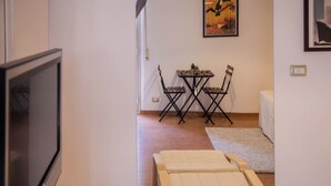 Una habitación con televisión, una cama, una mesita con sillas y un cartel en la pared.