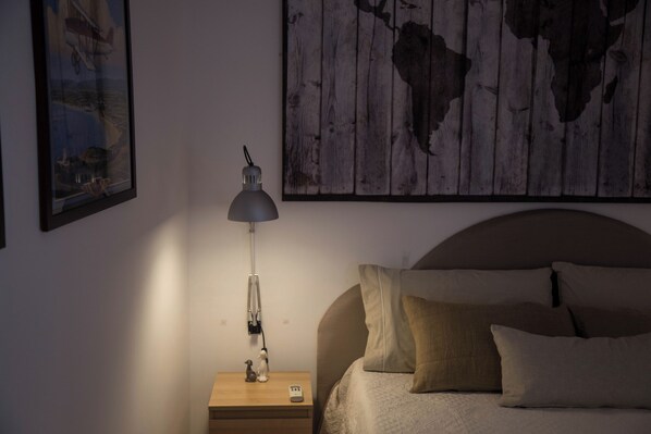 Een slaapkamer met een bed, een nachtkastje, een lamp en een lijst met een afbeelding aan de muur.
