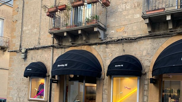 Un edificio con toldos arqueados, macetas con plantas y un escaparate con un maniquí.
