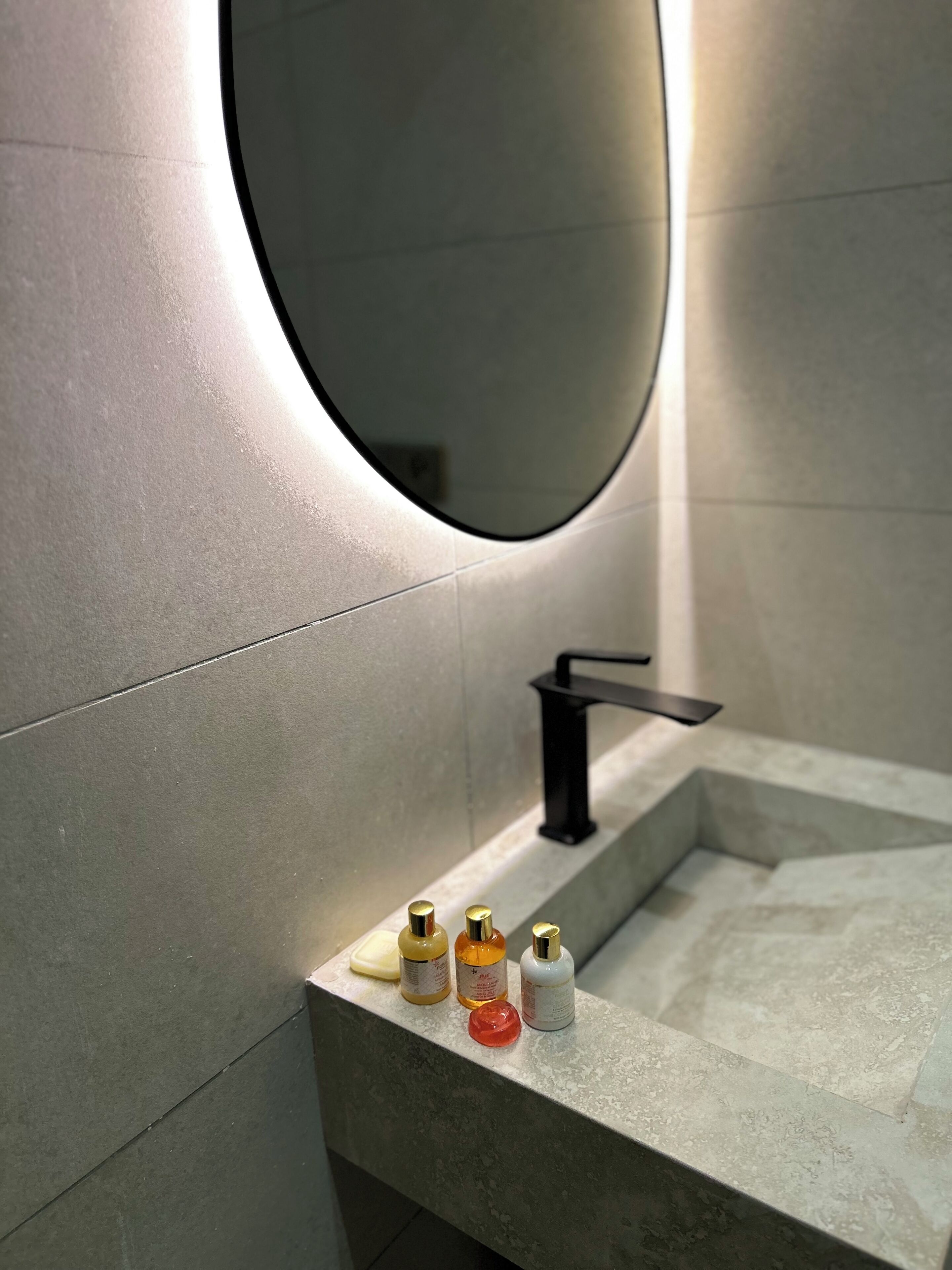 Une salle de bain moderne avec un grand miroir, un robinet noir et trois articles de toilette posés sur le comptoir.