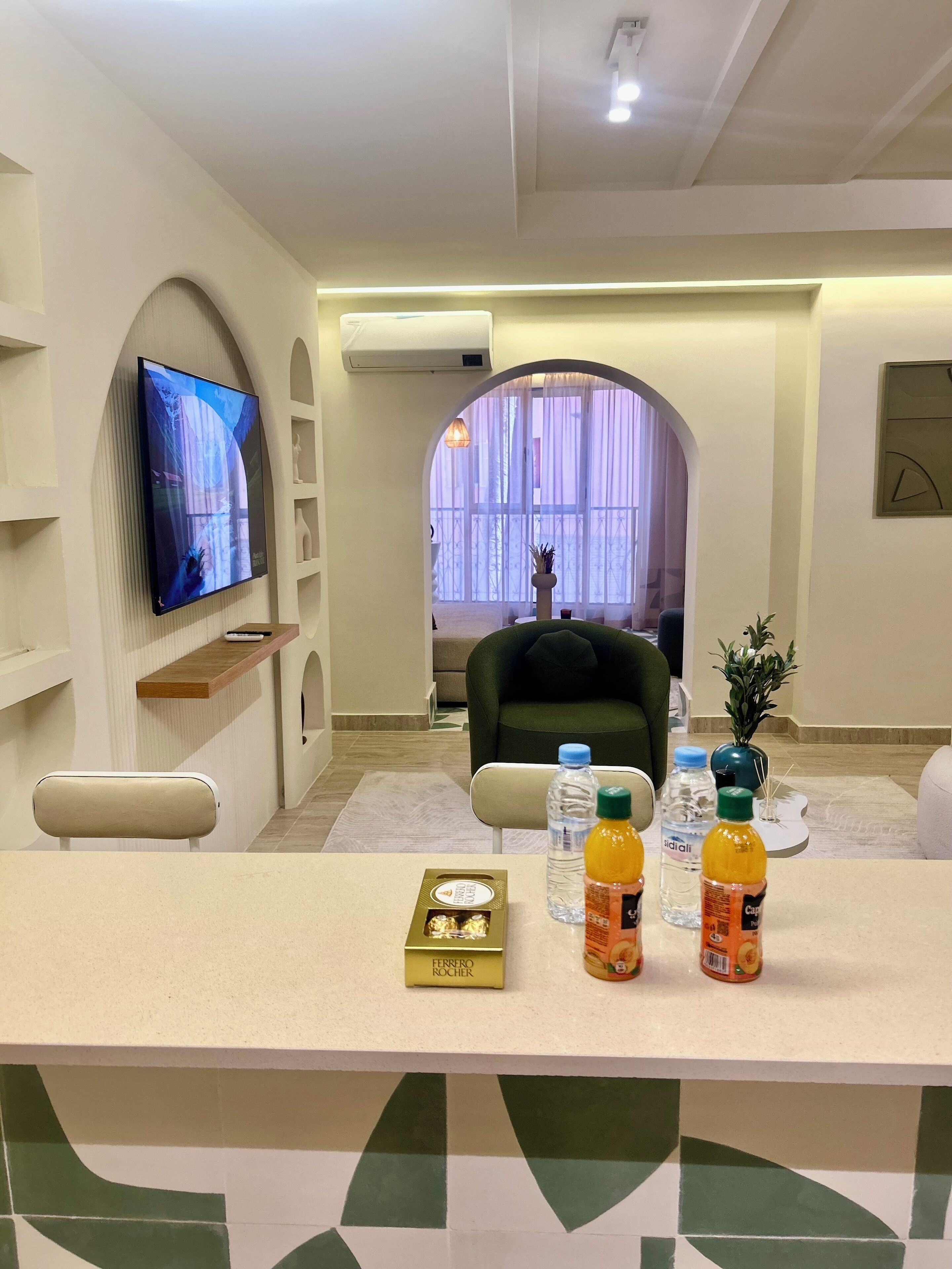 A modern living room with a flat-screen TV mounted on the wall, a comfortable sofa, and a coffee table with water bottles and snacks.