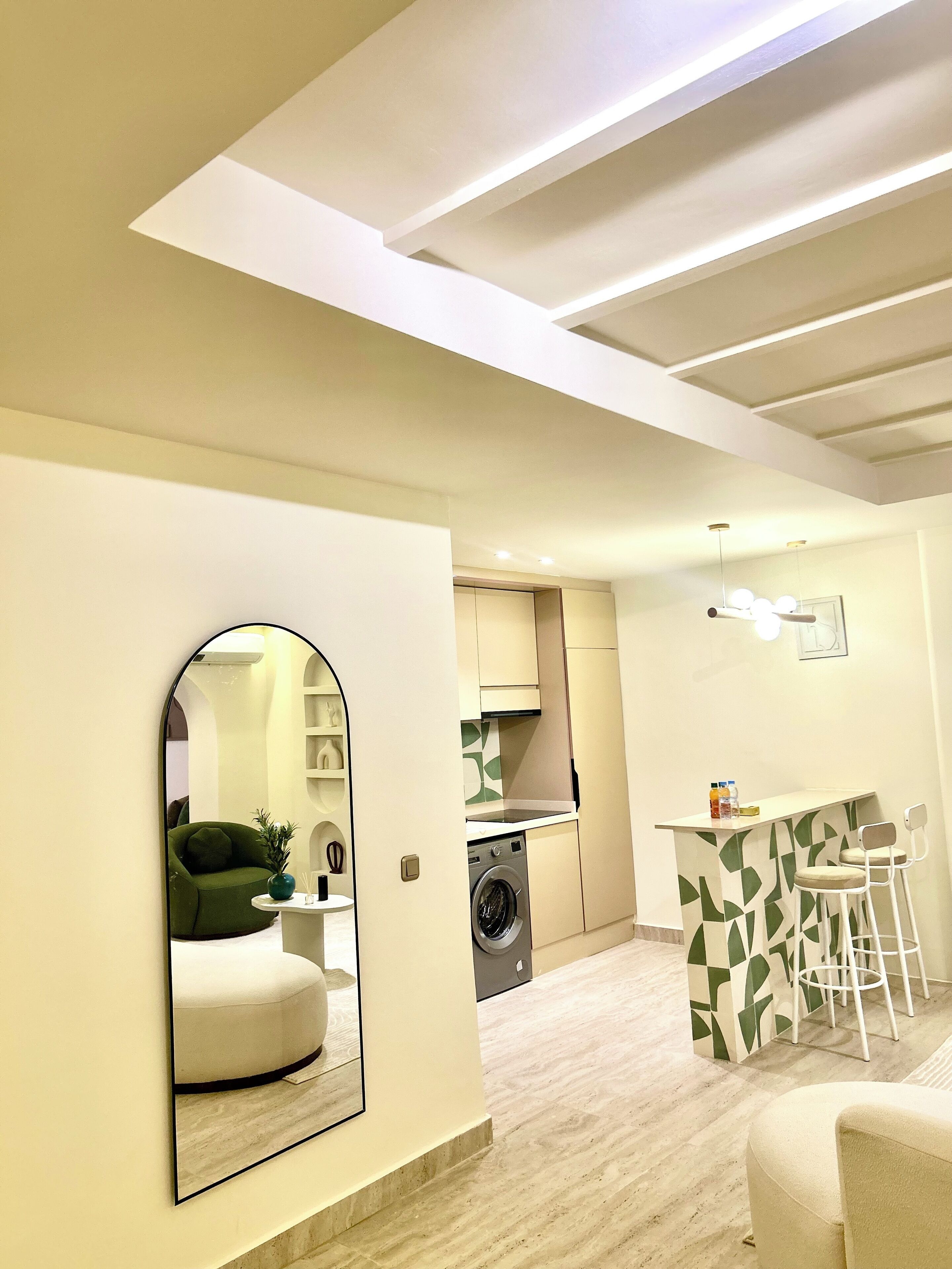 A compact living space with a kitchen, a washing machine, a dining area with bar stools, and a mirrored wall.