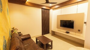 A modern living room with a brown leather sofa, a wooden coffee table, and a flat-screen TV mounted on the wall. - Kaizen Residency (Tiruchirappalli)
