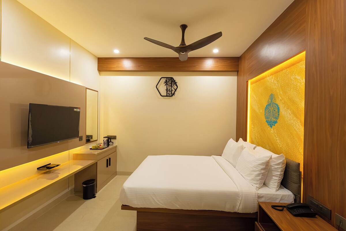 A modern hotel room with a bed, bedside table, TV, and a ceiling fan.
