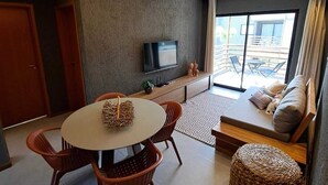 Un salon moderne avec une table à manger ronde, deux chaises, un canapé, un téléviseur et un balcon avec vue.