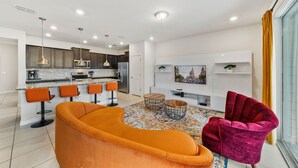Ein modernes Wohnzimmer mit einem gebogenen orangefarbenen Sofa, einem roten Samt-Sessel und einem an der Wand befestigten Fernseher.