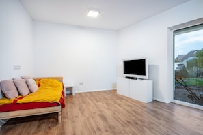 Ein modernes Schlafzimmer mit einem hölzernen Bett, einem Flachbildfernseher und einem großen Fenster mit Blick auf eine Wohngegend.