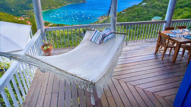 A hammock on a wooden deck with a table set for dining, overlooking a coastal landscape with boats and greenery. - NEW LISTING: Makere House, Cottage & Pool - Spectacular Views, 5 Mins To Beaches (Cane Garden Bay)