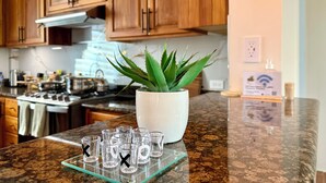 A kitchen with wooden cabinets, a white pot with a green plant, and a glass tray with empty shot glasses. - Diamond-Convenient Spa bath condo with ADA access (Mt Pleasant)