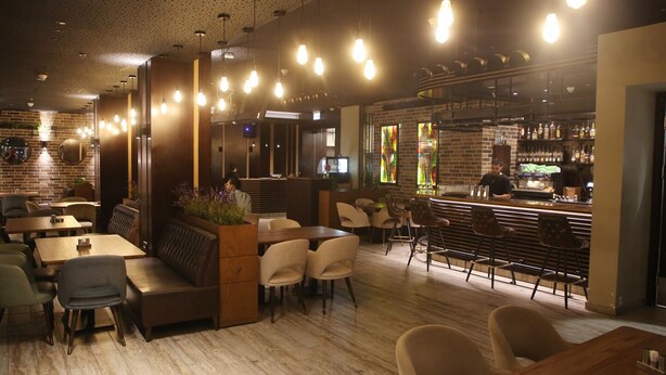 A restaurant with wooden tables and chairs, a bar area, and a brick wall. - Saint Francis Hotel (Bethlehem)