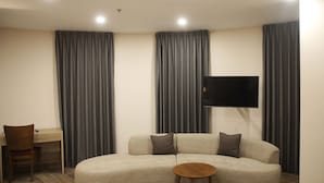 A modern living room with a sofa, a small round table, a TV mounted on the wall, and a desk with a chair. - Saint Francis Hotel (Bethlehem)