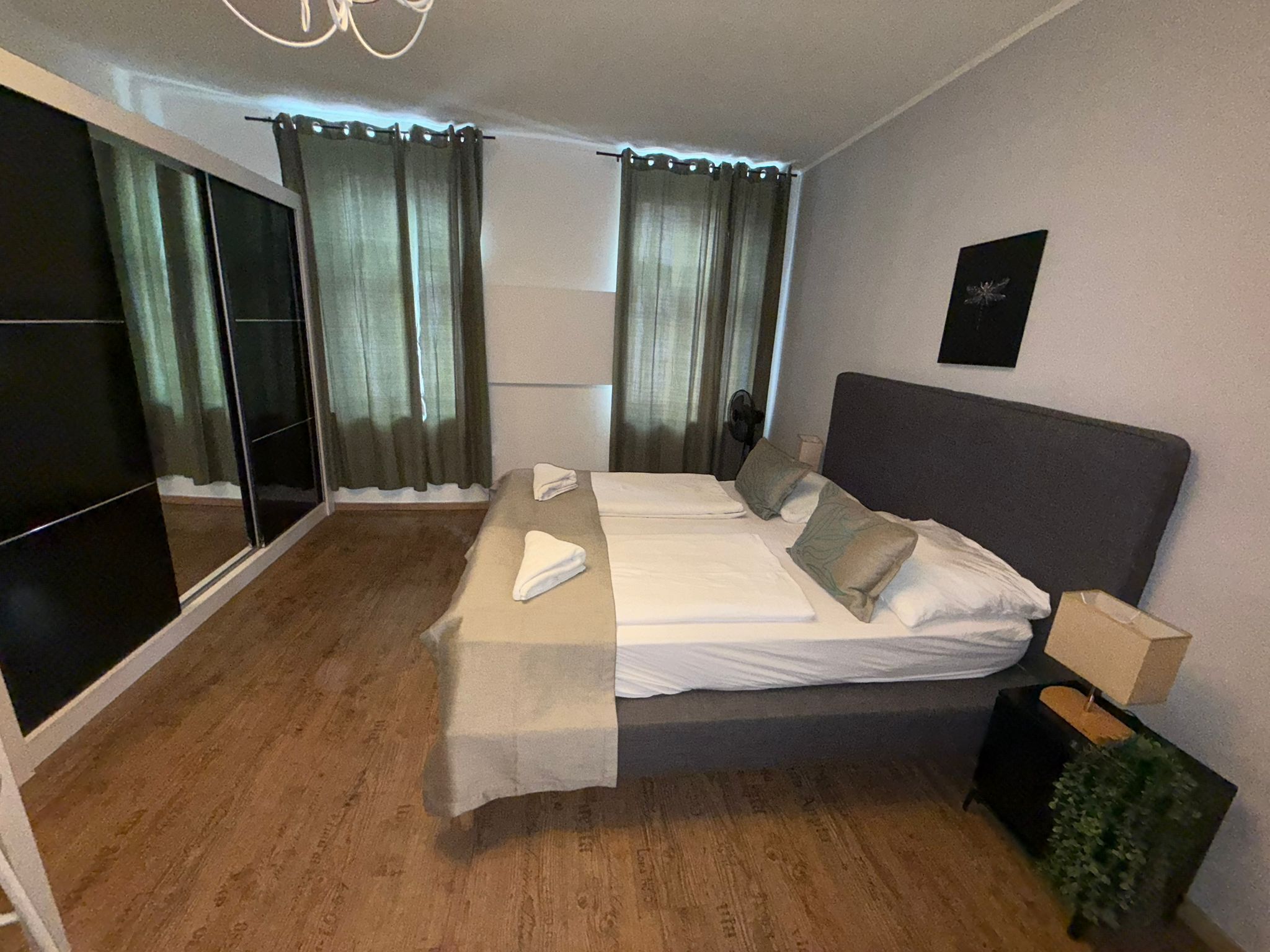Moderni hotellihuone, jossa on suuri sänky, yöpöytä, peili ja liukuovi, joka johtaa parvekkeelle.