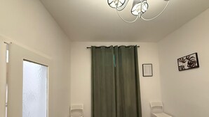 Ein Zimmer mit Holzboden, einer weißen Tür, zwei weißen Stühlen, einem grünen Vorhang und einer Chandelier.