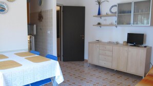 Ein Zimmer mit Esstisch, Stühlen, einem Fernseher auf einer Kommode und einem gemusterten Boden.