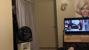 A bedroom with a bed, a TV displaying a show, a fan, and a door leading to a closet. - Studio apartment across the street from the convention center (San Diego)