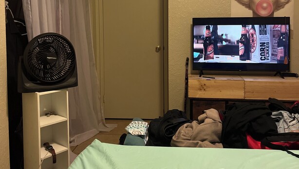 A bedroom with a bed, a TV on a wooden stand, a fan, and a door with a curtain. - Studio apartment across the street from the convention center (San Diego)