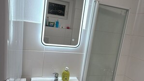 A bathroom with a white sink, a mirror, and a glass shower enclosure. - Economy Souterrain 2BR - Prater Amuesement Park (Vienna)