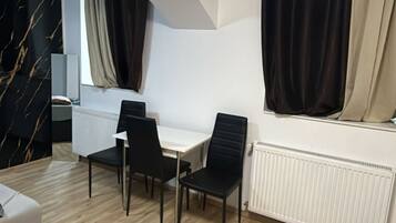 Ein moderner Raum mit einem weißen Tisch, schwarzen Stühlen, einer Heizung und einem Fenster mit Vorhängen.