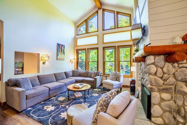 A spacious living room with a sectional sofa, a round coffee table, and a stone fireplace. - Pet Friendly 2+L/3BA W/ Views! Jacuzzi, W/D & BBQ (Mammoth Lakes)