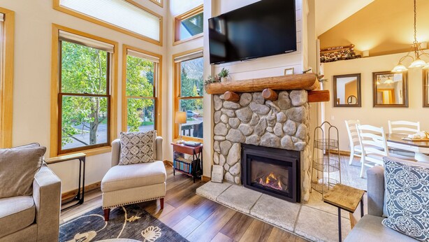 A spacious living room with a stone fireplace, large windows, and a flat-screen TV mounted above it. - Pet Friendly 2+L/3BA W/ Views! Jacuzzi, W/D & BBQ (Mammoth Lakes)