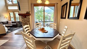 A dining area with a round table, white chairs, and a stone wall. - Pet Friendly 2+L/3BA W/ Views! Jacuzzi, W/D & BBQ (Mammoth Lakes)