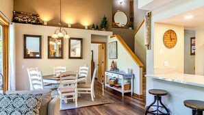 A spacious living area with a dining table, white chairs, a sofa, and a bar area with stools. - Pet Friendly 2+L/3BA W/ Views! Jacuzzi, W/D & BBQ (Mammoth Lakes)
