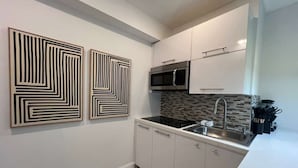 Cozinha moderna com armários brancos, bancada preta, micro-ondas e pia. Há duas obras de arte abstratas nas paredes.