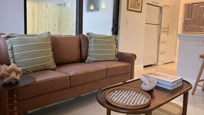 Uma sala de estar com um sofá marrom, almofadas listradas, uma mesa de centro redonda feita de material trançado e um livro.