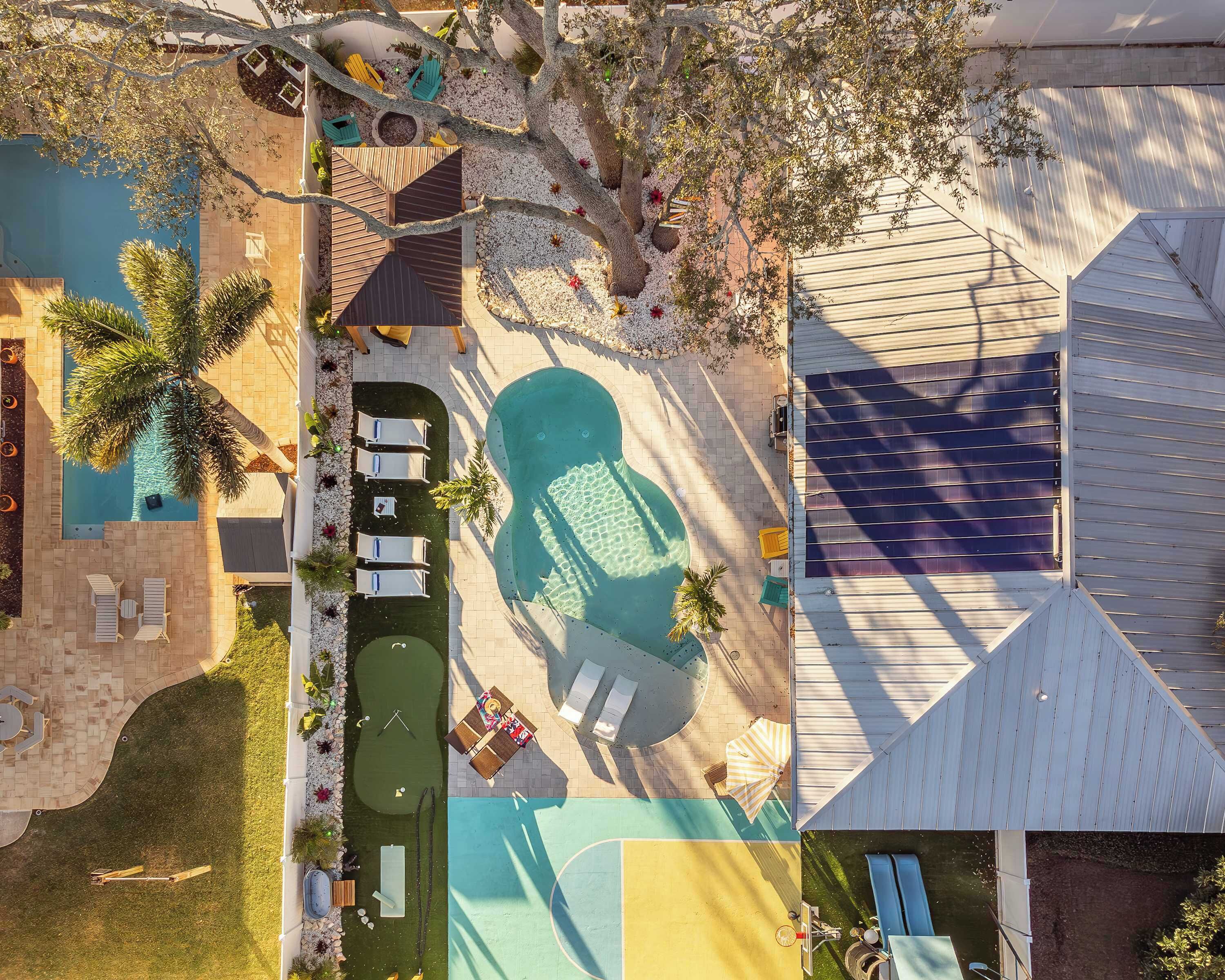 Oversigtsbillede af et resort med swimmingpool, liggestole, tennisbane og en overdækket terrasse.