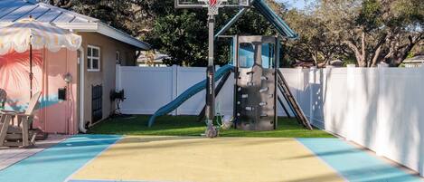 A basketball court with a hoop, a slide, and a climbing wall.