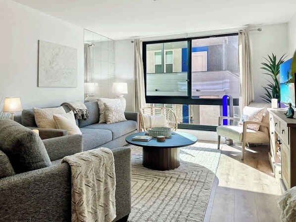 A modern living room with a grey sofa, a round coffee table, and a large window with a view of the outside.