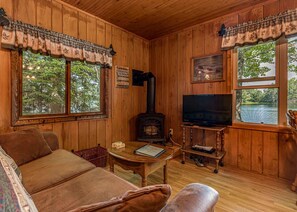 A cozy cabin interior with wooden walls, a fireplace, a television, and large windows overlooking a lake. - Bouchard Shores Resort - Your Private Northwoods Getaway (Minocqua)