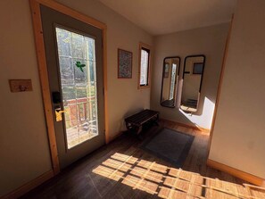 Ein Zimmer mit Holzboden, einer Bank, einer Tür mit Ausblick nach draußen und zwei gerahmten Bildern an der Wand.