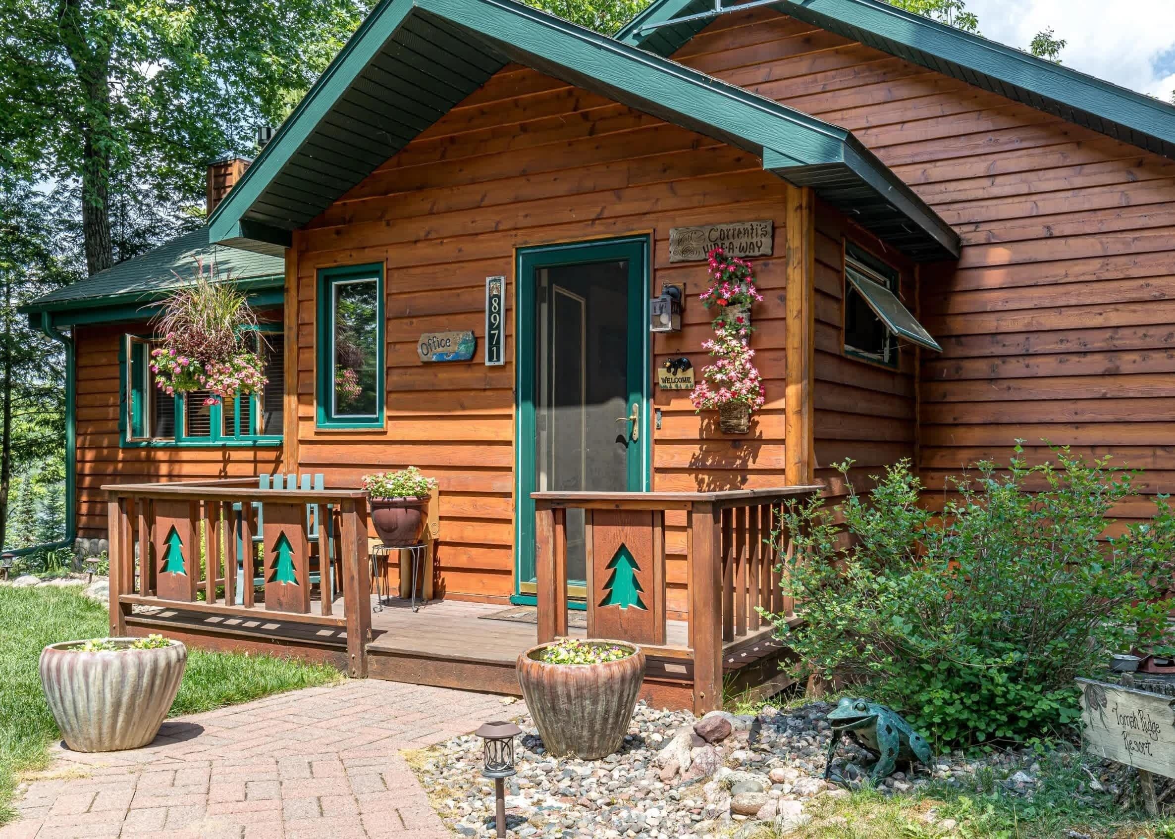 A wooden cabin with a porch, a welcome sign, and a sign indicating it's a campsite.