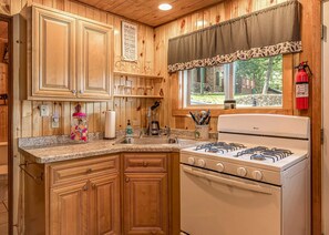 Une cuisine avec des meubles en bois, une cuisinière à gaz, un évier et une fenêtre donnant sur un paysage verdoyant.