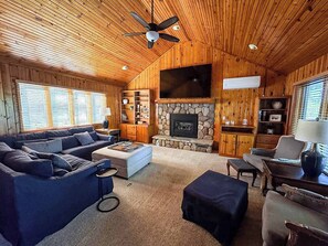 A cozy cabin interior with a stone fireplace, wooden walls, a large TV, and a ceiling fan. - Bouchard Shores Resort - Your Private Northwoods Getaway (Minocqua)