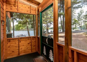 Una cabaña con un ventanal grande con vista a un lago, paredes de madera y una puerta con portón de metal.