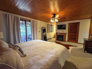 Un dormitorio con una cama grande, techo de madera, ventilador de techo, chimenea y televisor montado en la pared.