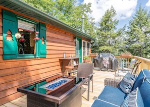 Eine Holzterrasse mit Gartenmöbeln, einem Grill und einem Glastisch mit blauen Steinen.
