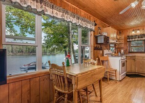 A cabin with a wooden interior, a dining table with chairs, a kitchen area, and large windows overlooking a lake. - Bouchard Shores Resort - Your Private Northwoods Getaway (Minocqua)