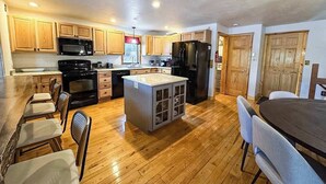 A spacious kitchen with wooden cabinets, a central island, and a dining area with a table and chairs. - Hilltop - Bouchard Shores Resort (Minocqua)