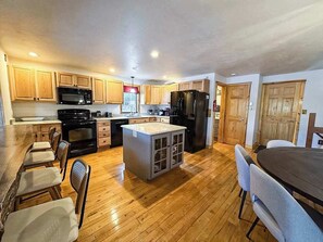 A spacious kitchen with wooden cabinets, a central island, and a dining area with a table and chairs. - Hilltop - Bouchard Shores Resort (Minocqua)