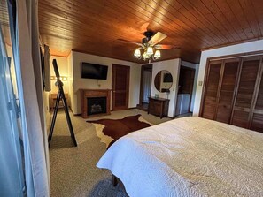 A bedroom with a large bed, a ceiling fan, a fireplace, and wooden walls. - Hilltop - Bouchard Shores Resort (Minocqua)
