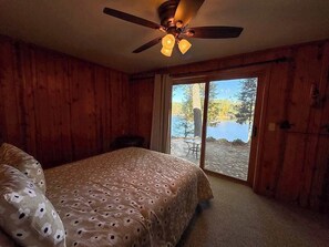 A bedroom with a bed, a ceiling fan, and a view of a lake through a sliding glass door. - Hilltop - Bouchard Shores Resort (Minocqua)