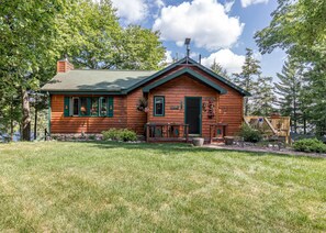 Une cabane en bois avec un toit vert, une véranda à l’avant avec une table et des chaises, et une petite terrasse.