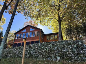 A wooden cabin with a stone wall in front, surrounded by trees. - Hilltop - Bouchard Shores Resort (Minocqua)