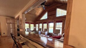 A kitchen with a long wooden counter, bar stools, and a seating area with chairs and a sofa. - Hilltop - Bouchard Shores Resort (Minocqua)