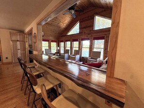 A kitchen with a long wooden counter, bar stools, and a seating area with chairs and a sofa. - Hilltop - Bouchard Shores Resort (Minocqua)