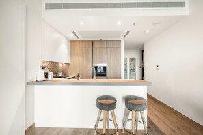 Une cuisine moderne dotée d’un îlot central, de meubles en bois, d’appareils électroménagers en acier inoxydable et de deux tabourets de bar.