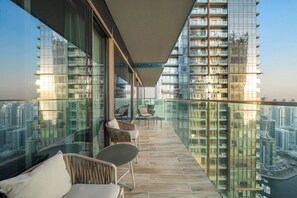 Un balcon doté de balustrades en verre, de meubles en osier et offrant une vue sur le paysage urbain.